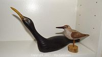 Side view of two bird carvings showing long black loon neck and smaller shore bird mounted on wood base.