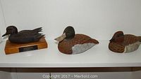 Three hand carved wooden duck sculptures displayed on a shelf, showing all items in the lot.