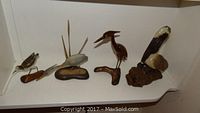 Wide view of the full collection of five hand crafted bird figurines displayed on a white shelf.