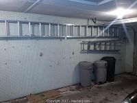 Long aluminum extension ladder mounted horizontally on wall above trash bins.