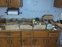 Wide view of boxes of assorted nails, screws and hardware on wooden cabinet with pegboard background.
