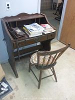 Full view of small wooden desk, vintage chair, Western Electric push button phone on desk, assorted manuals stacked on top of desk.