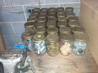 Thirty-nine glass jars filled with assorted hardware such as screws, bolts, nuts, washers, placed on a wooden shelf.