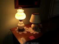 Milk glass hurricane lamp and ceramic floral lamp illuminated on a wooden table with doily beneath