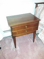 Full view of one Willett nightstand showing two drawers, bronze hardware, and tapered legs on carpet.