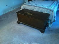 Chest placed on carpet in front of a bed showing overall view including top, sides, base and positioning.
