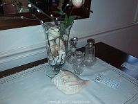 Photo showing three perfume bottles and one glass vase on a table with shells inside the vase.
