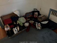 Photo showing assortment of ladies shoes arranged in front of luggage and various handbags around on floor, including a white hat.