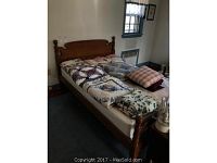 Wooden full bed frame with headboard, footboard, and rails. Bed has multi-colored quilts and pillows on mattress.