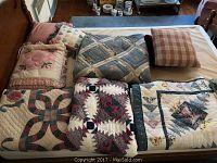 Full view of four quilts and four throw pillows laid on a bed, showcasing patterns and colors.