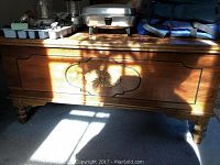 Front view of wooden cedar chest with carved floral decoration showing wear marks on top surface.