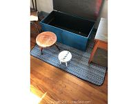 Dark striped rectangular rug laid on wood floor with storage chest and stools on it.
