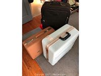 Three suitcases positioned on floor: black rolling suitcase at back, tan vintage suitcase and white vintage suitcase at front.
