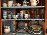 Shelf with multiple pieces of dishware and glassware including cups, plates, bowls, and glasses.