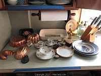 Overview of kitchen counter with copper molds, espresso set, platters, brass ducks, and Wolfgang Puck knife set