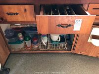 Open kitchen cabinet containing dozens of assorted plastic containers and lids placed on shelves and in racks.