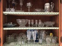 Three shelves of varied clear glassware including bowls, candy dishes, cordial and whiskey glasses arranged inside a wooden cabinet