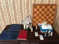 Wide view of the chess pieces of plastic and ceramic sets and wooden chess board, also albums stacked on the side.