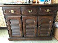 Front view showing three top drawers with brass handles and three louvered cupboard doors below with brass knobs.