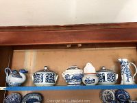 Shelf with six blue and white ceramic pieces including duck teapot, three lidded serving dishes, candle stand, and tall pitcher