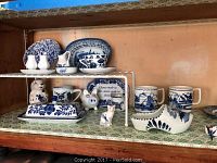 Photo of blue and white ceramic mugs, plates, small dishes, butter dish, animal figurines, and a wooden shoe on a shelf
