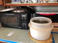 Sharp black Sharp Carousel microwave with digital keypad and glass front door, next to round plastic storage bins with lids on kitchen counter.