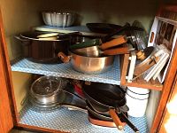 Two shelves inside a cabinet filled with various pots, pans, mixing bowl, and glass bakeware.
