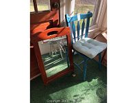 Vintage wooden framed mirror leaning against door next to vintage blue painted wooden chair with beige cushion.