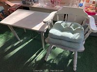 Image showing the vintage wooden table and small armchair with cushions from a side angle, illuminated by sunlight.