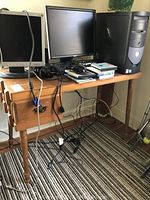 Wooden vintage desk with computer monitors and accessories on top, showing the overall structure and condition of the desk including legs and drawer.