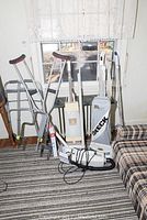Photo showing the metal walker, tub support, set of crutches, Oreck vacuum cleaner with gray bag, Sears carpet and floor conditioner on a striped carpet.