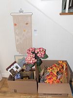 Fall-themed decor items including a Happy Autumn fabric wall hanging, pink faux floral bouquet, autumn leaf wreaths, and a box of small framed paintings and signs.