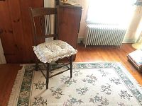 Full view of the vintage wooden chair with floral seat cushion placed on the area rug, showing the room background and wood floor.