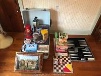Overview of collection showing vintage collectible tins, board games stacked, backgammon game set opened, and hardshell suitcase behind them