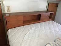 Full view of the headboard showing wooden finish and shelving compartments with sliding doors.