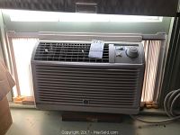 Front view of GE window air conditioner showing grille, control panel with rotary dial, and installed in window frame.