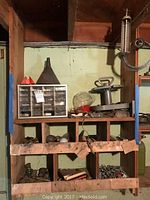 Three shelves filled with various hardware items including a small plastic drawer cabinet, metal balls, hinges, and other assorted metal parts.