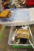 Two large plastic storage tubs, one with blue lid open showing various items inside, including a carved wooden box, glass jars, and a yellow box labeled EZ Moves.