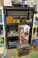 Four-shelf black plastic shelving unit with assorted tools and boxed Shop Vac and Quick Vac items on shelves and floor around unit.