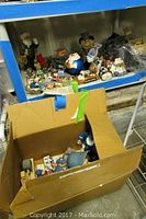 Wide view of shelf and box containing US Postal themed figurines including a large postal stuffed bear and multiple smaller collectible figures.