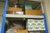 Top portion of plastic shelving showing various items including a wooden box labeled 'Salad Set' and a musical cake plate.