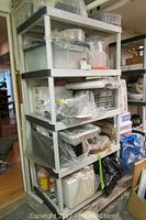 Wide view of the plastic five-shelf storage unit filled with various kitchenware items packed in plastic bags and containers.