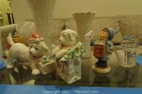 Photo showing two Lenox dog figurines, Goebel Hummel postman, and Fenton glass teddy bear in front of two Lenox white vases on a glass table.