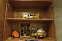 Full view of wooden shelf with the ceramic NY Taxi cookie jar, the DVD movie Taxi, several small metal taxi models, and a yellow and black stationery item