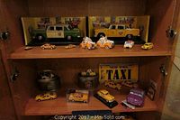 Two shelves displaying assortment of miniature taxis, salt and pepper shakers, and clocks with tins. Includes boxed Sun Star Checker cabs, Home Spike shakers, Fossil clocks, and other yellow taxis.