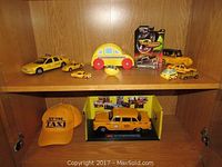 Shelves displaying multiple yellow miniature taxis, a yellow New York Taxi embroidered ball cap, and other taxi collectibles including boxed items and a wooden toy taxi with red wheels.