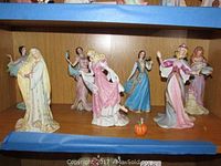 Eight Lenox porcelain princess figurines displayed on a shelf with protective blue paper framing the shelf edges