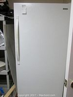 Full view of closed upright Kenmore freezer in white color, showing handle and label on top left corner of door.