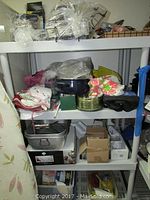 Plastic shelving unit with various kitchenware and linens on four shelves, including a large roasting pan, boxed butter dish, and linens.