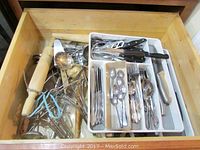 Drawer filled with assorted kitchen utensils such as wooden rolling pins, metal spoons, ladles, and a cutlery tray containing flatware and knives.